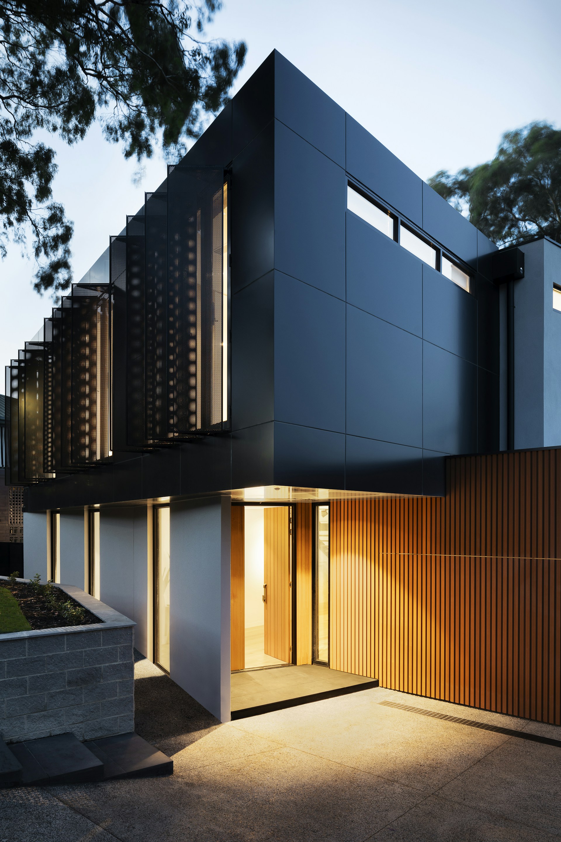 Modern dark-clad home with timber entry at dusk
